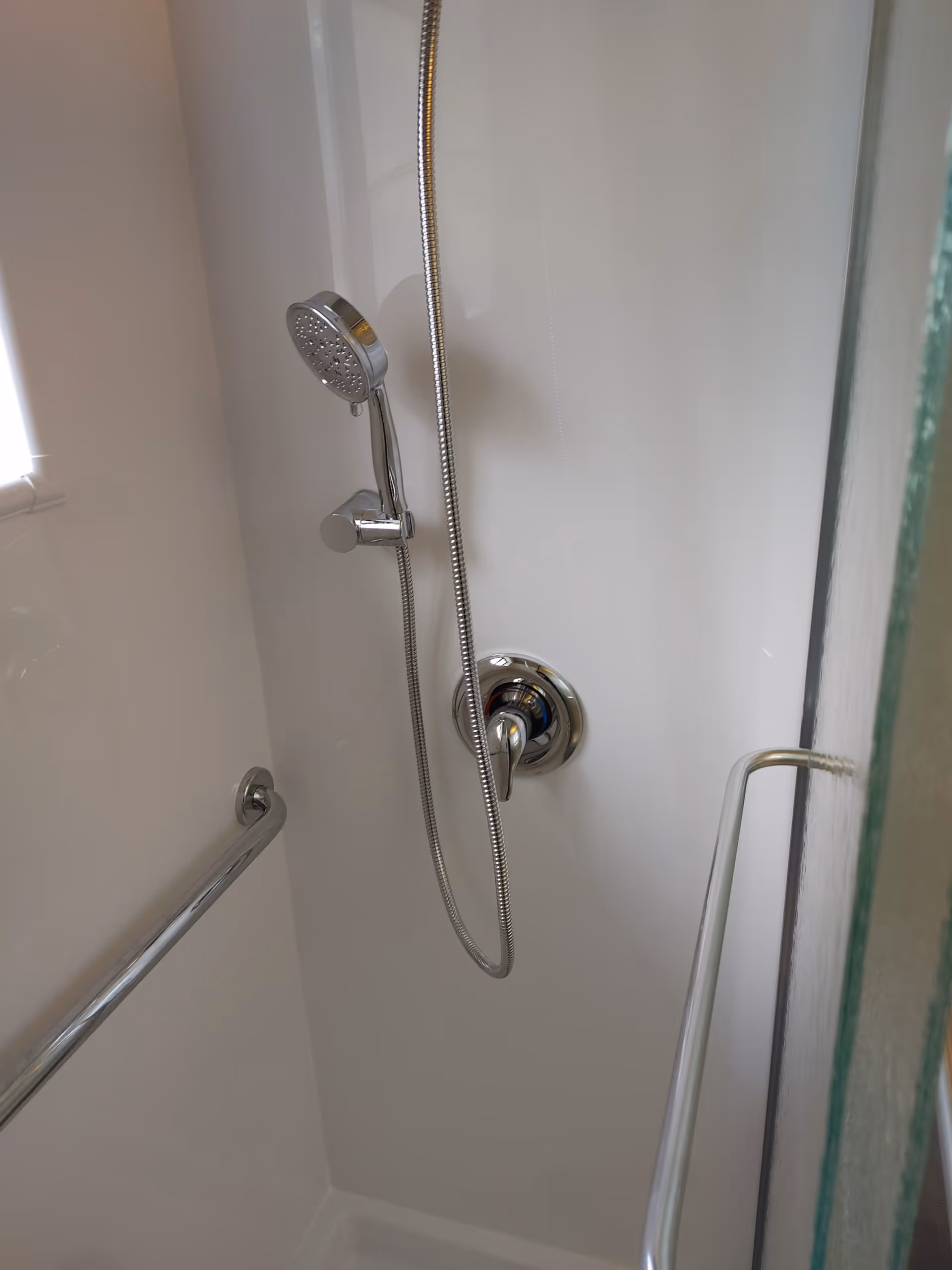 Shower stall with handheld showerhead, chrome fixtures, and a safety grab bar.