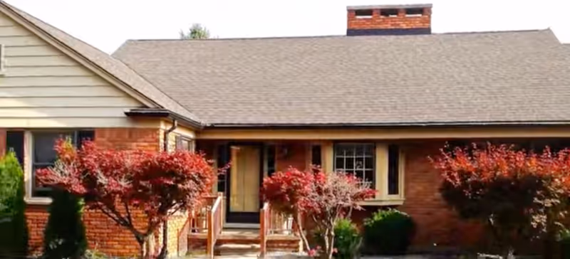 Brick, single-story lodge with entrance steps and red-leaved trees.