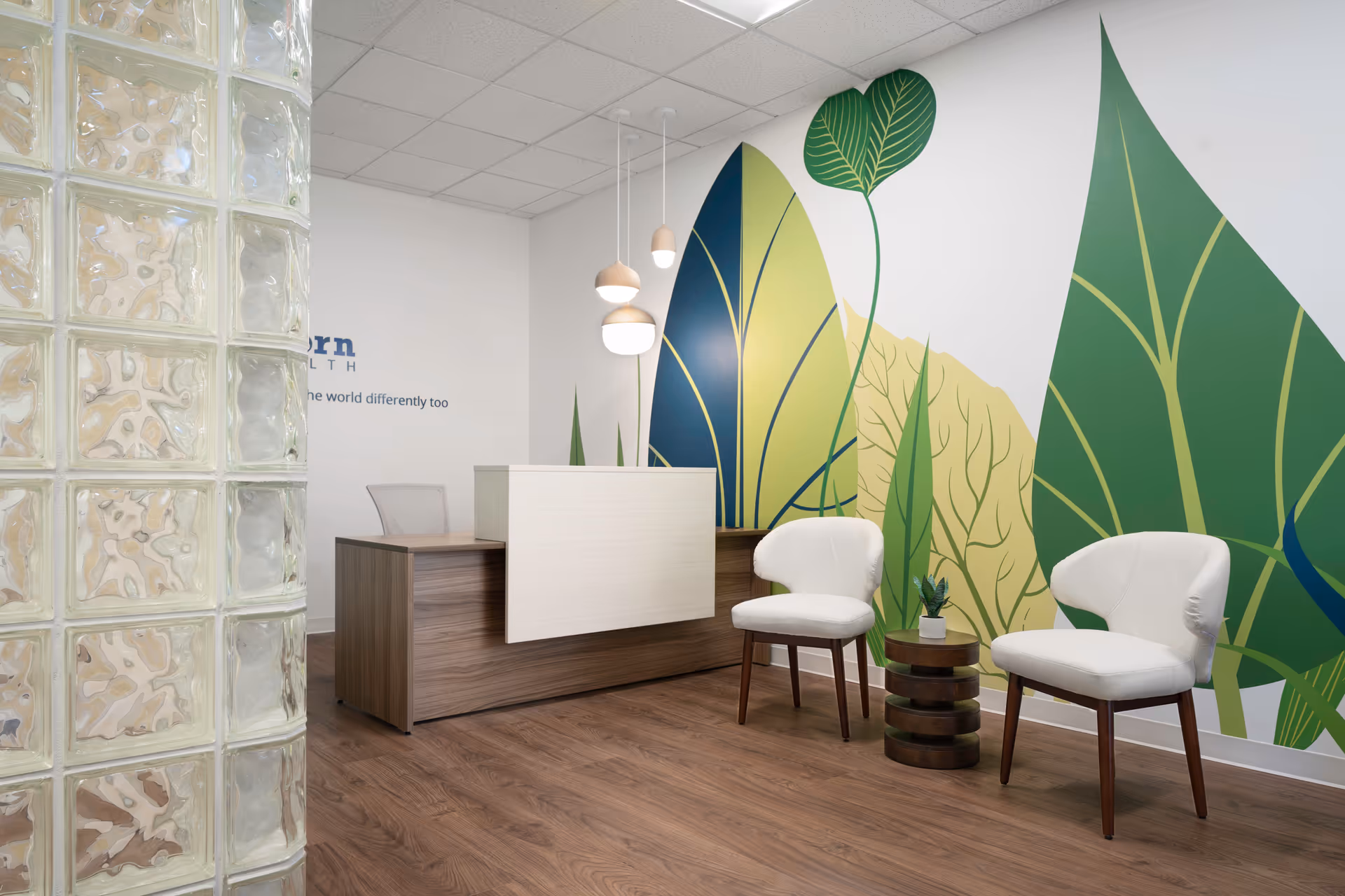 Reception area with a wood desk, leafy mural, and white chairs in a modern clinic.