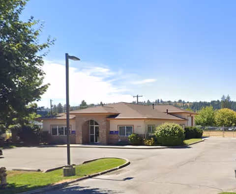 Single-story facility building with parking lot and landscaped entrance under a blue sky.