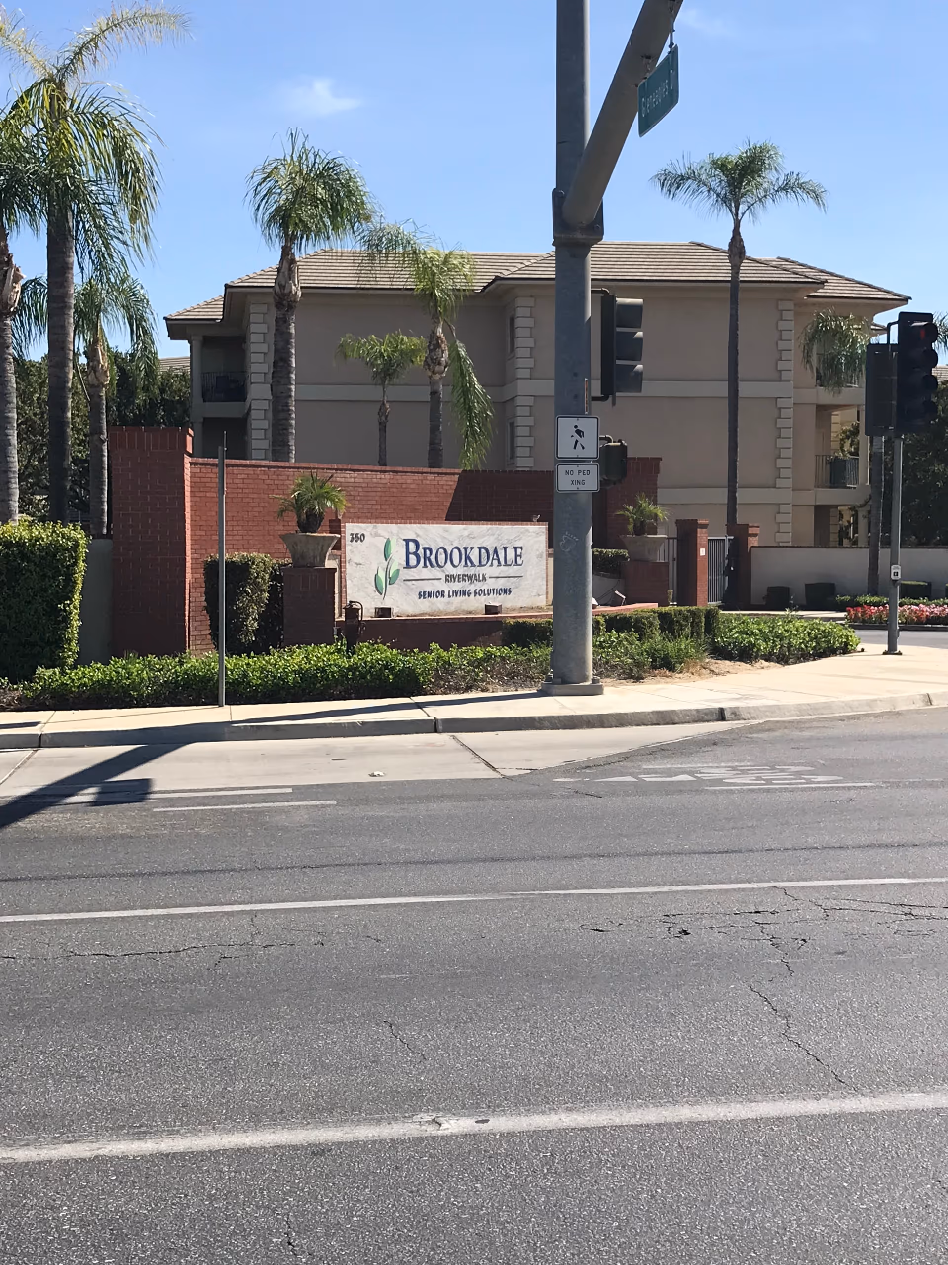 Exterior view of Brookdale Riverwalk senior living facility with palm trees and a sign.