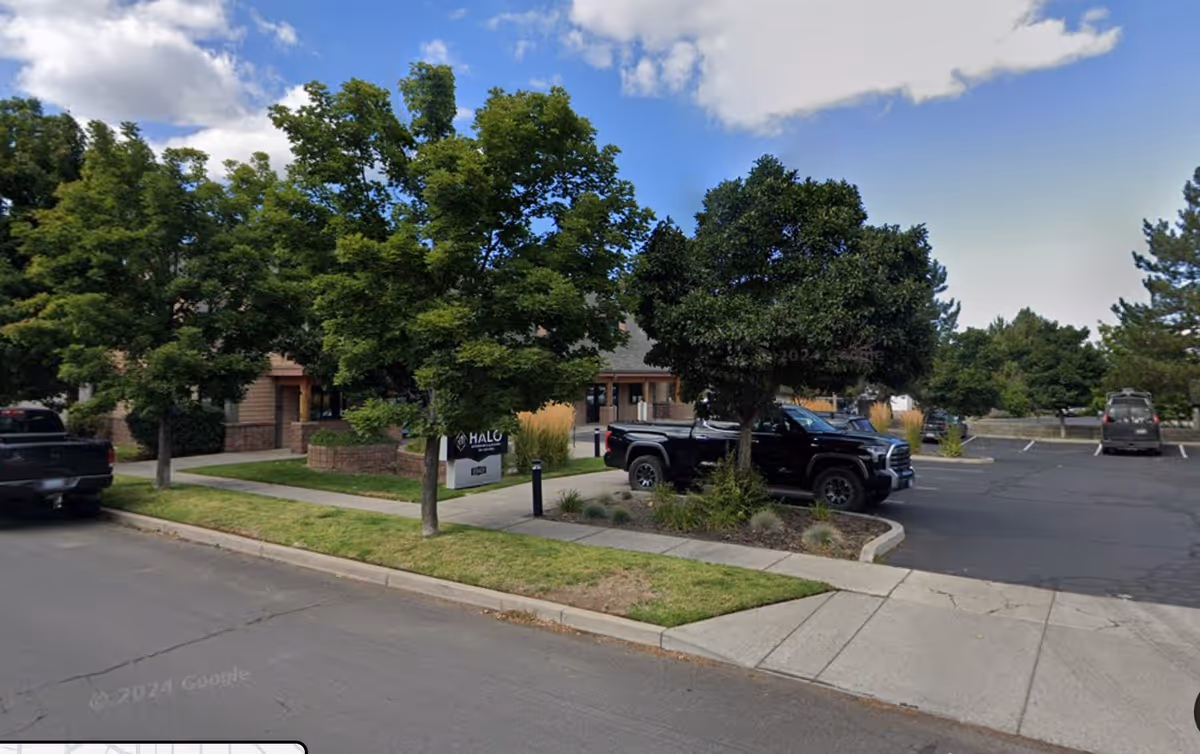 Exterior view of a senior living facility with trees and parked cars.