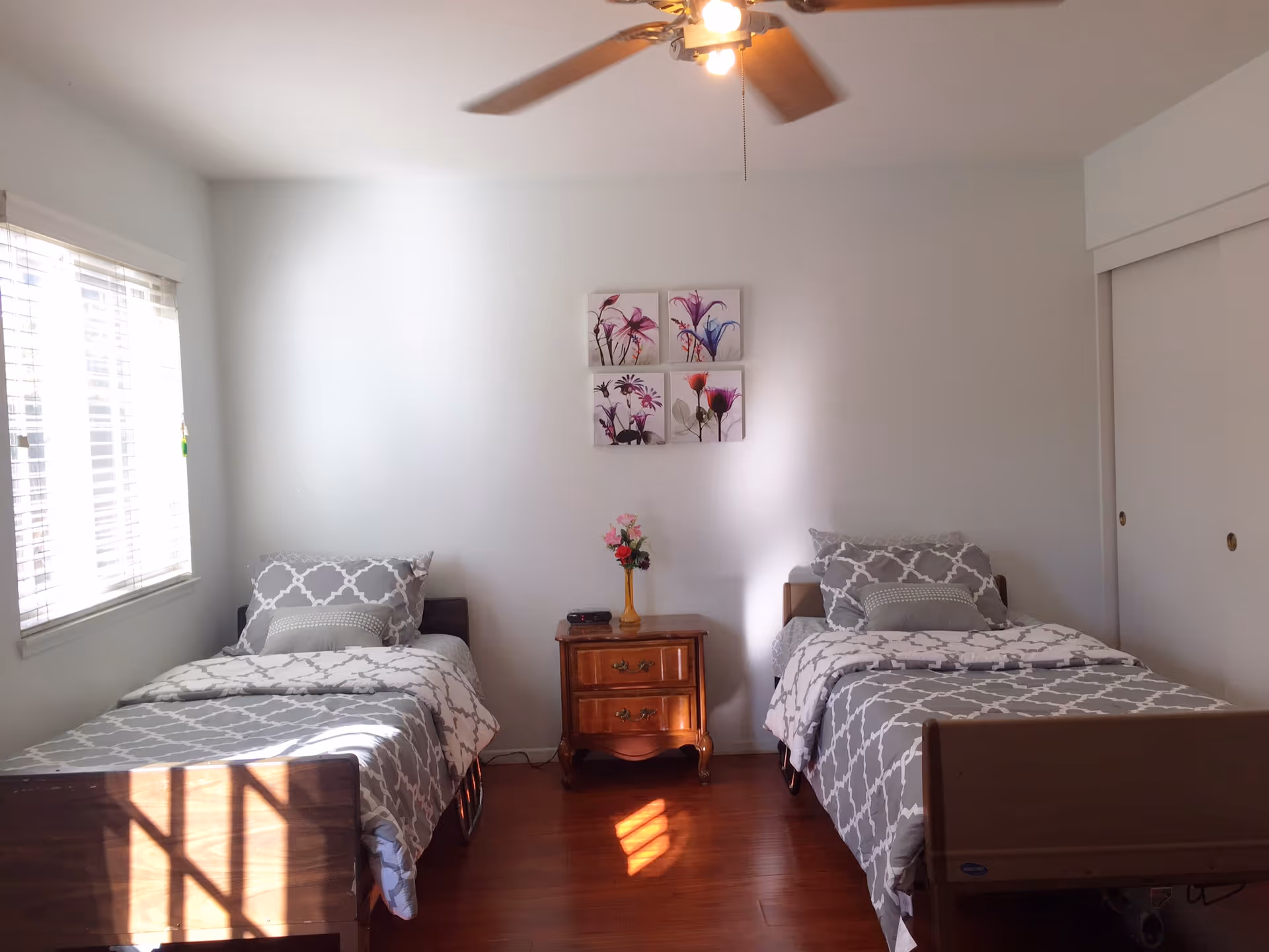 Bright bedroom with two twin beds, a wooden nightstand, and a ceiling fan.