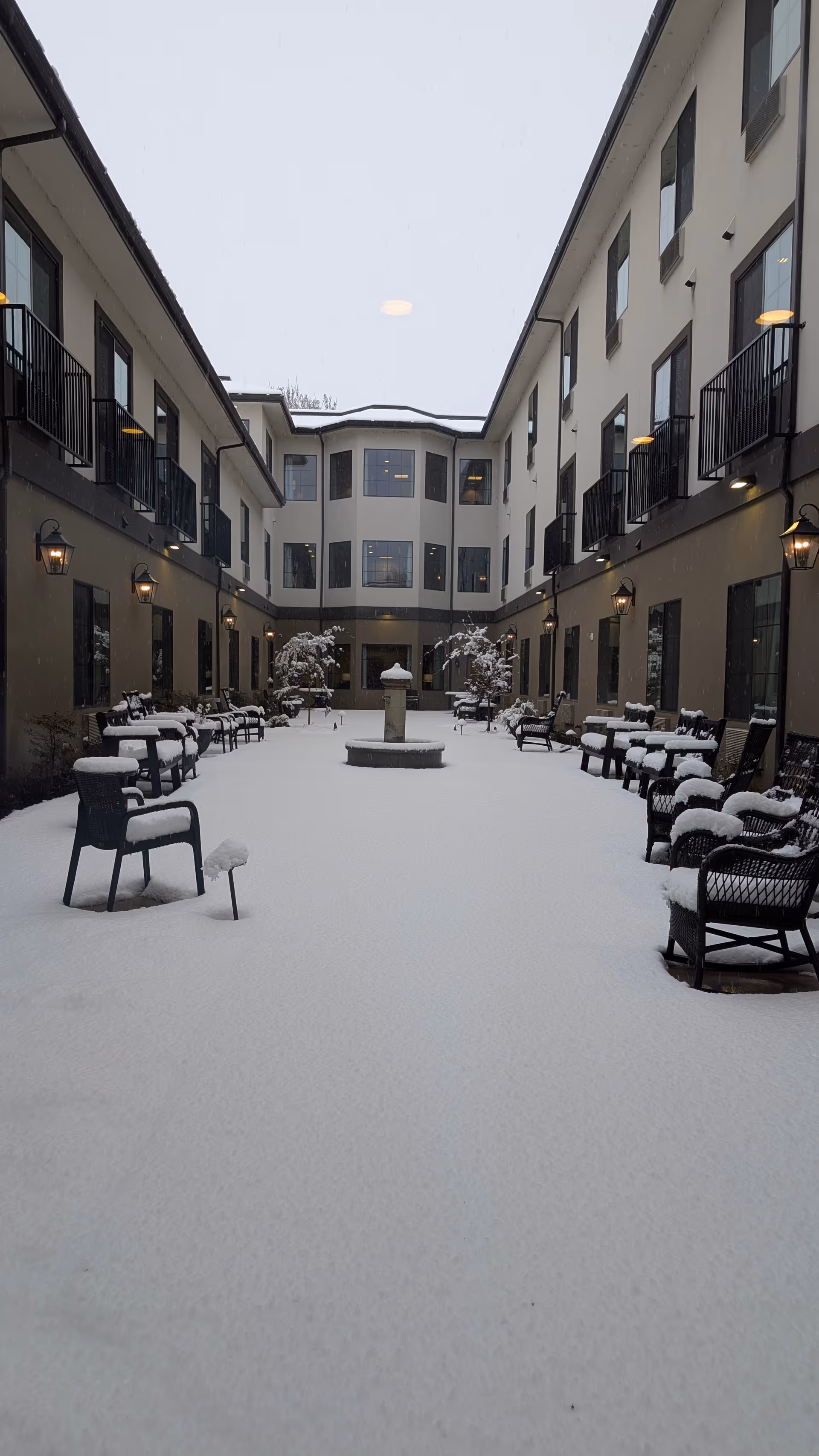 Snow-covered courtyard between two wings of Weatherly Court with benches and a fountain.