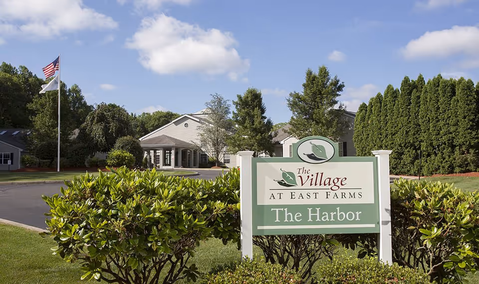 Exterior view of The Village at East Farms with a sign and landscaped entrance.