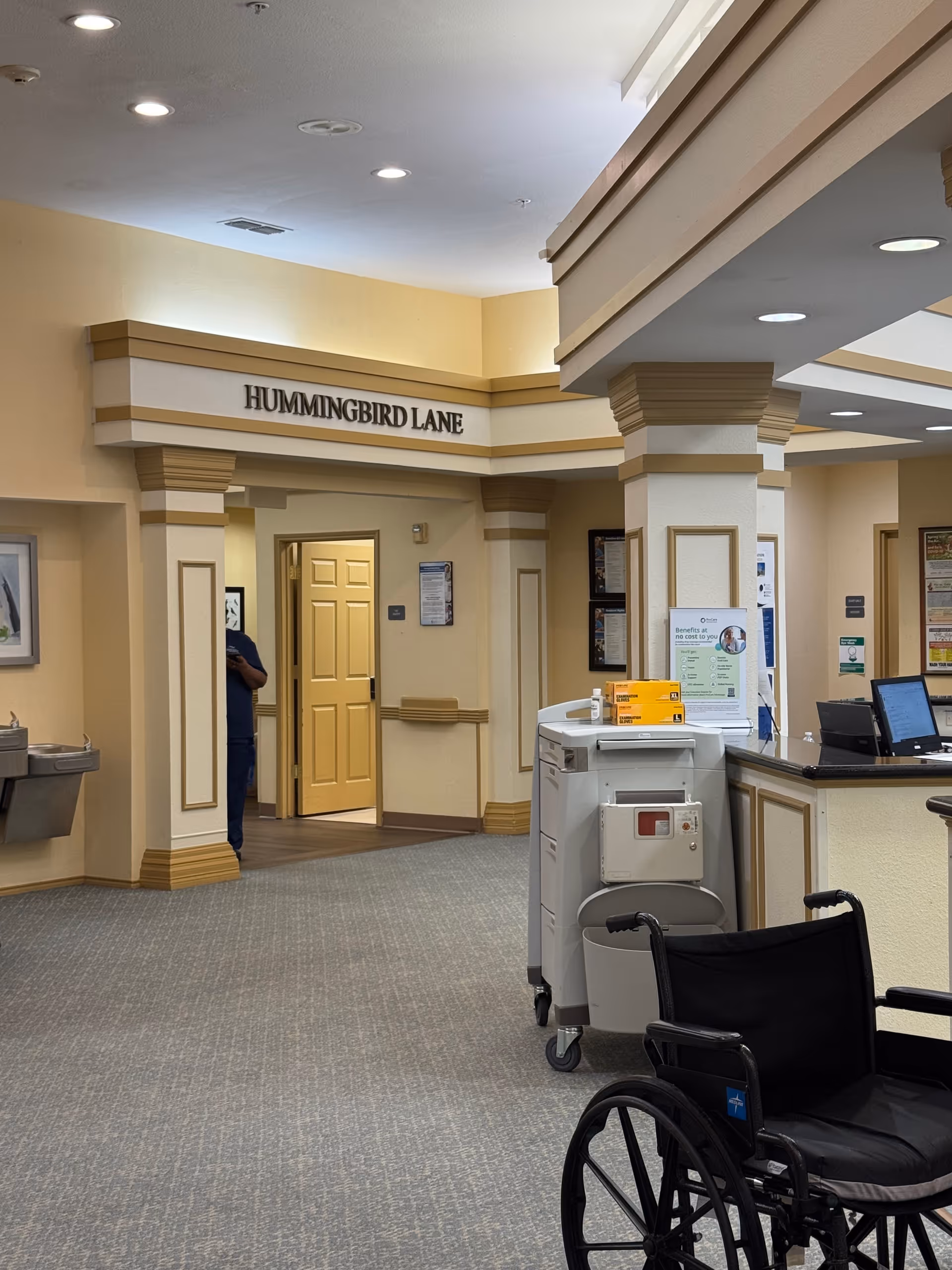 Lobby area with a reception desk, wheelchair in foreground, and Hummingbird Lane sign.