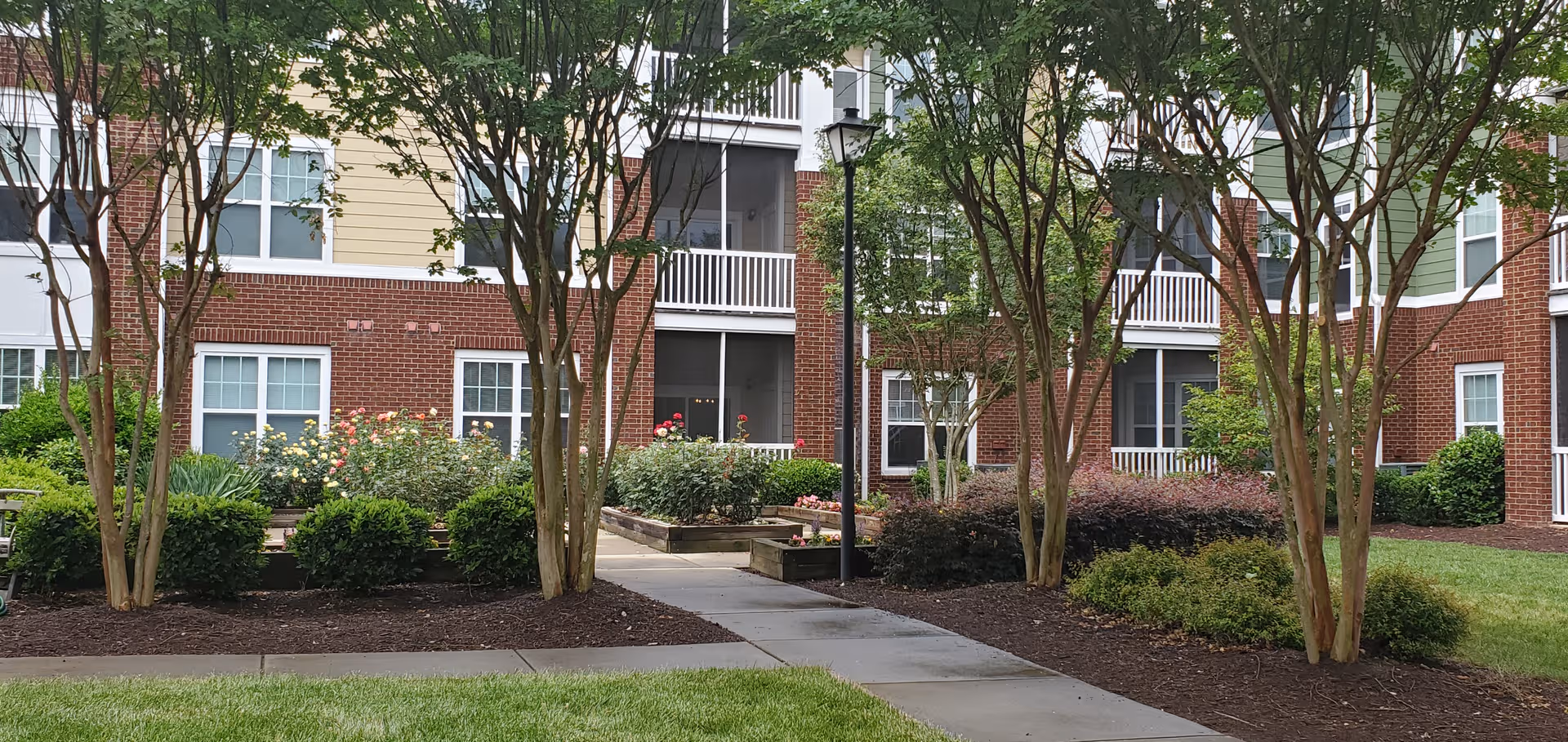 Exterior view of a brick senior living building with a landscaped front yard.