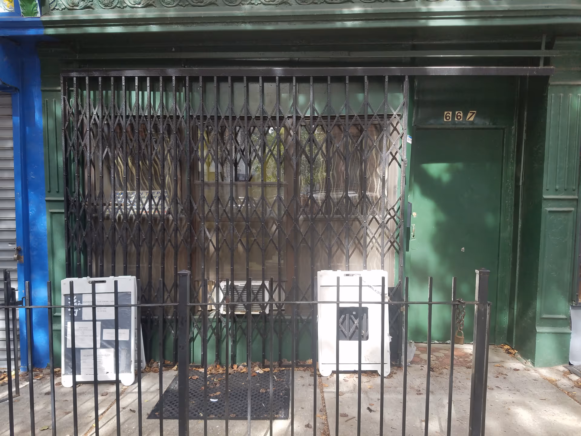Green door behind a crisscross metal gate, storefront with railing and sidewalk in front.