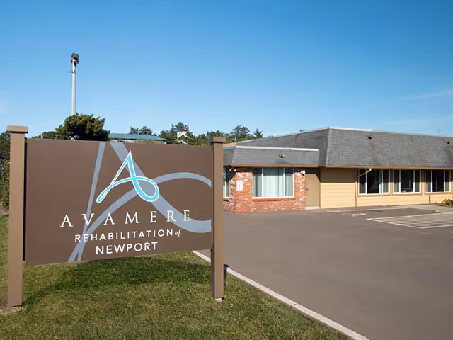 Outdoor view of the Avamere Rehabilitation of Newport sign in front of the facility building and parking lot under a clear blue sky.