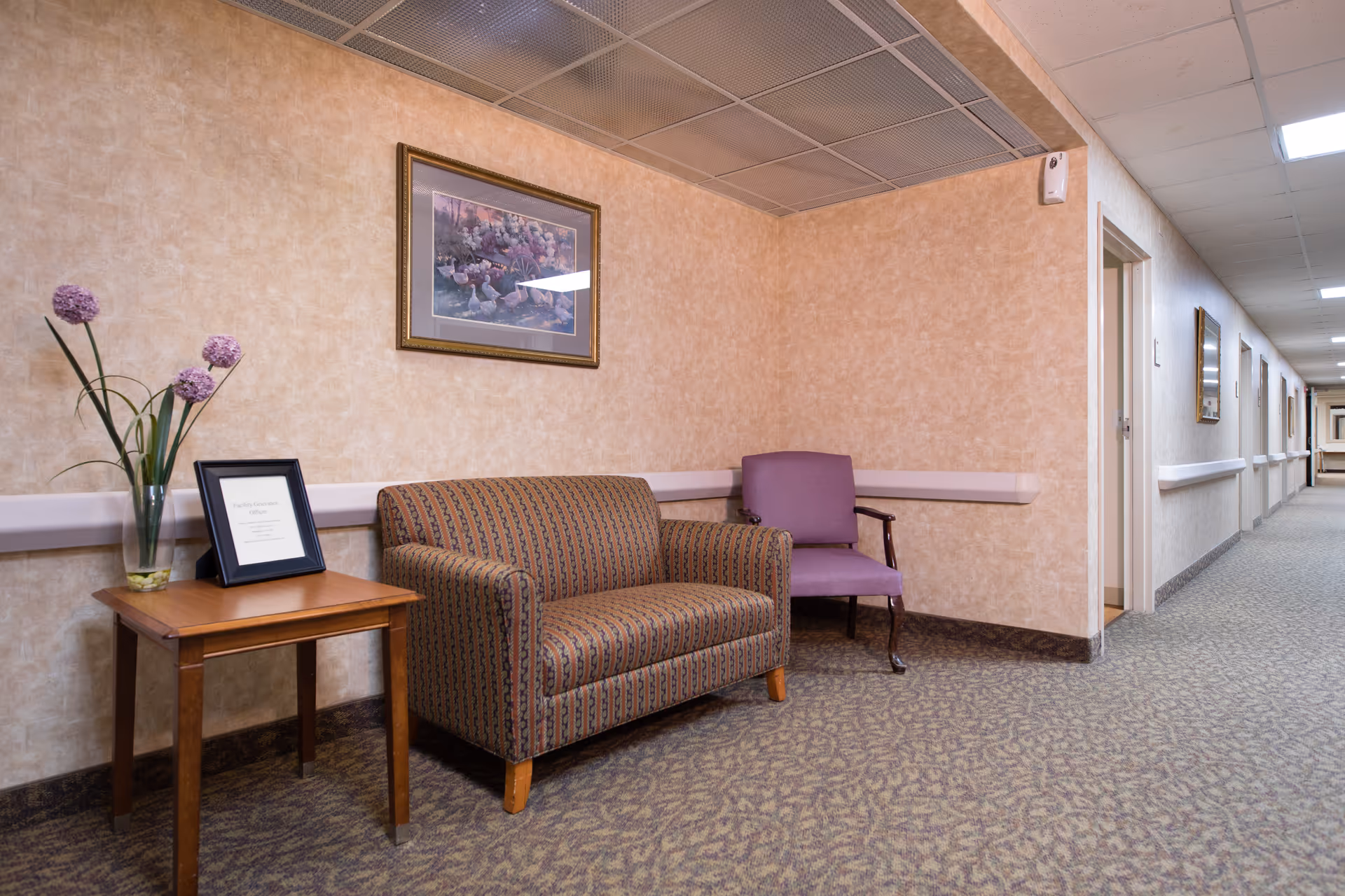 Peach-walled hallway seating area with sofa, purple chair, side table, and framed artwork.