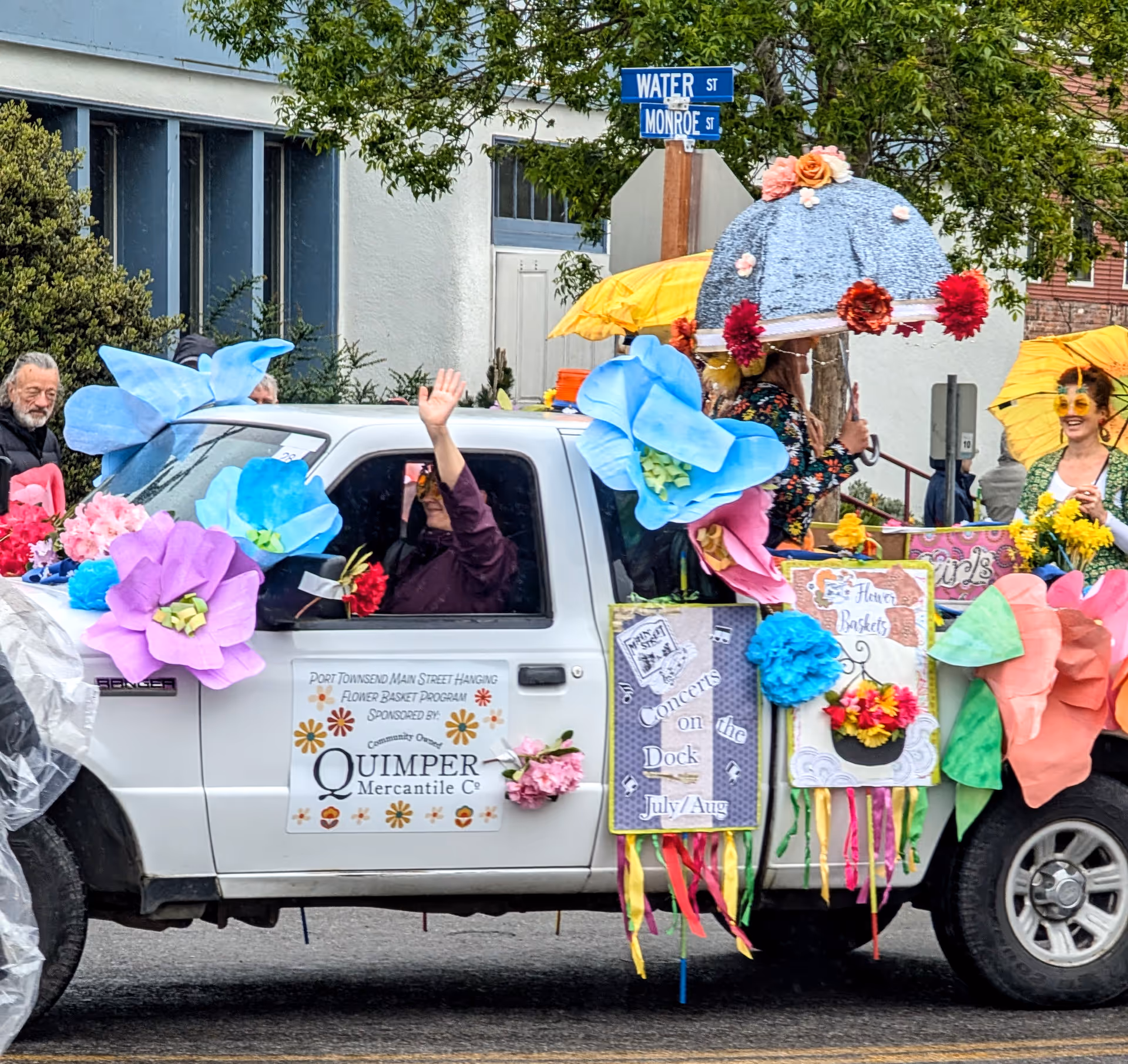 A decorated white pickup truck parading down a street with oversized paper flowers and umbrellas.