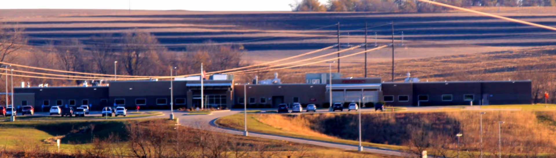 Long, low, single-story facility with a curved driveway and parked cars.
