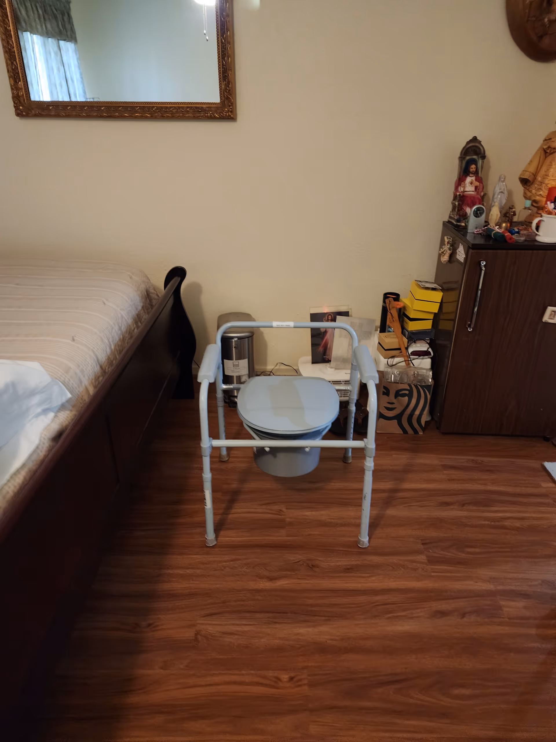 A bedroom with a bed, a mobility commode, and a cluttered dresser.