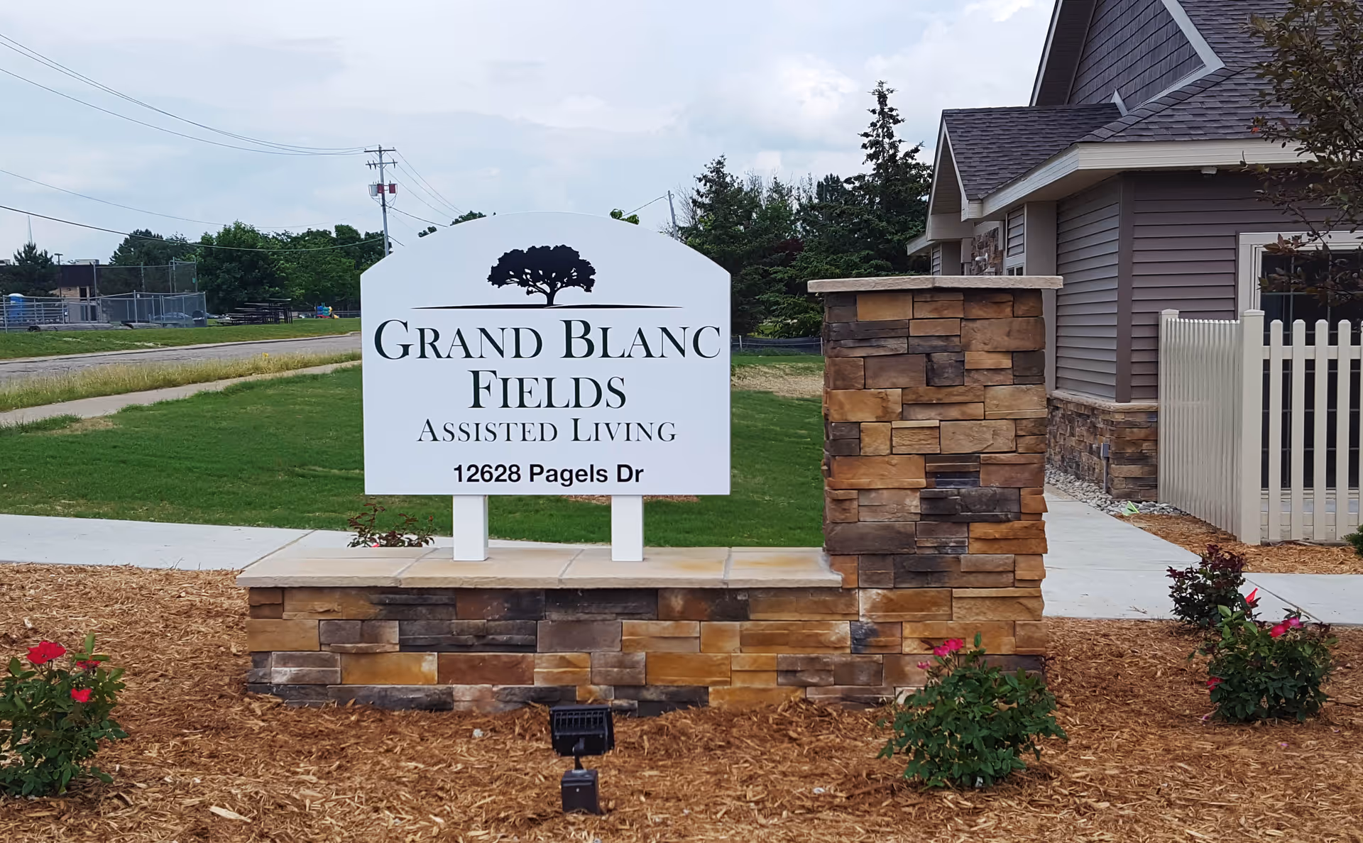 Exterior view of Grand Blanc Fields Assisted Living sign beside a stone pillar.