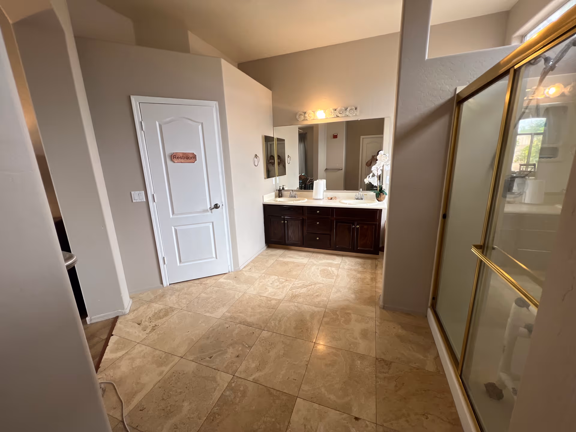 Facility bathroom with dual-sink vanity, mirror, shower stall, and tiled floor.