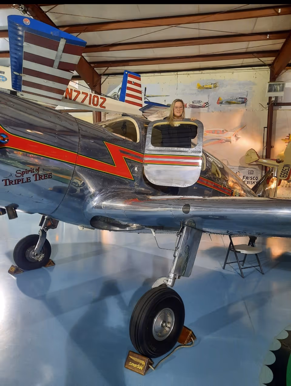 Inside a hangar, a vintage airplane on display with a person in the cockpit.