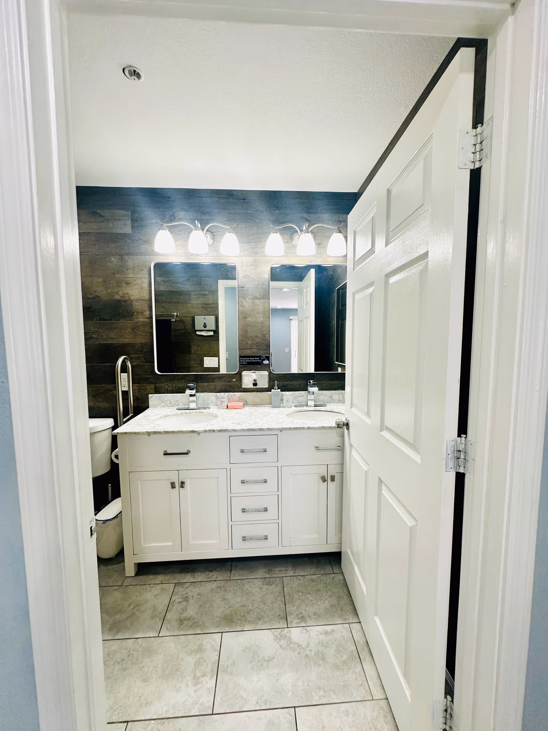 Bright bathroom with double-sink vanity, mirrors, and modern lighting, white cabinetry.