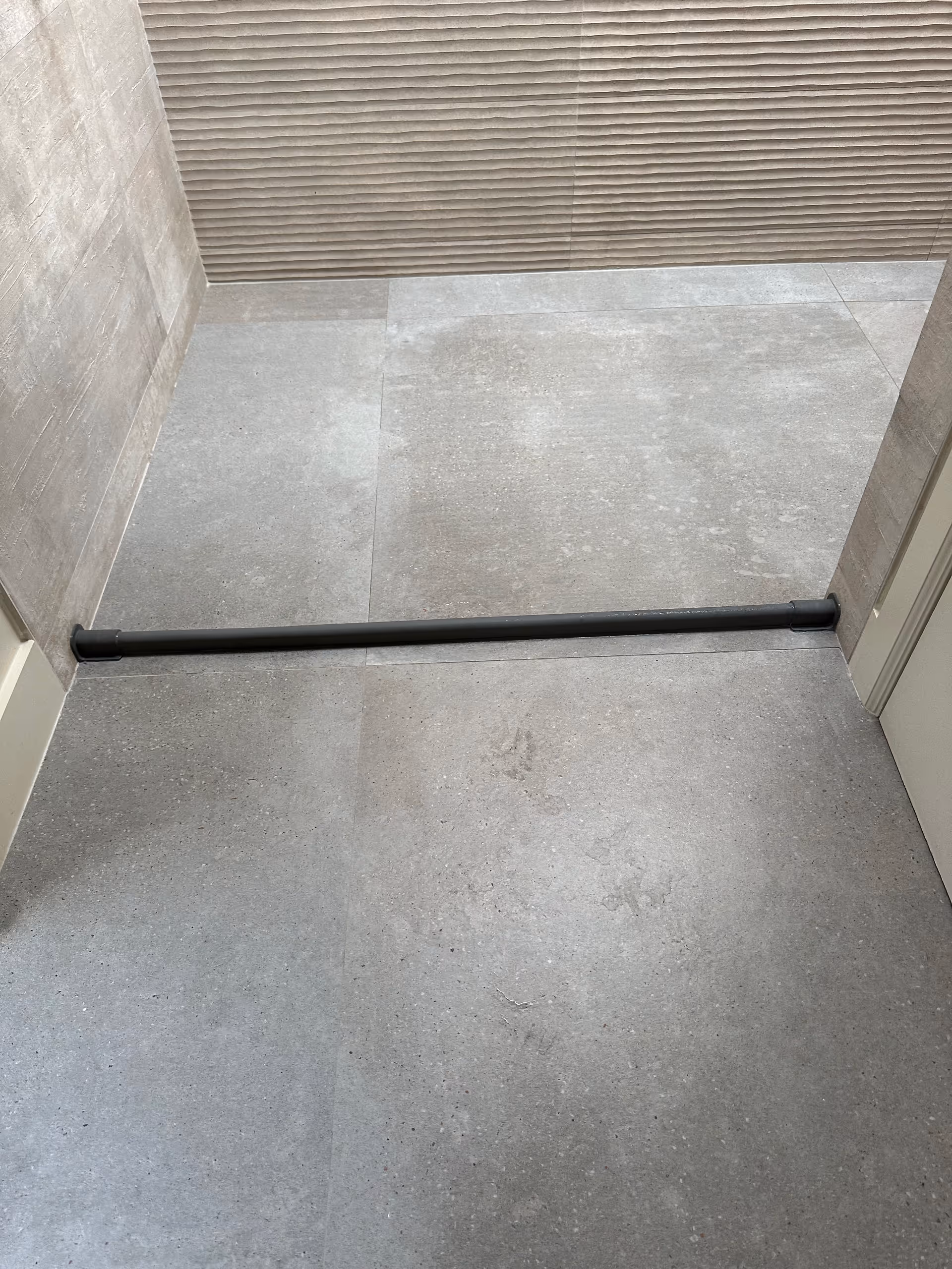 Empty hallway or elevator interior with grey tile walls and a black rail across the floor.