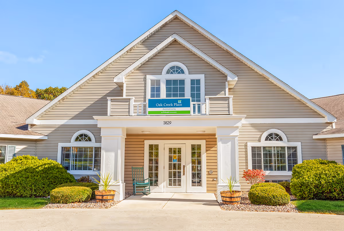 Senior living facility front entrance with beige siding, arched windows, and landscaped shrubs.