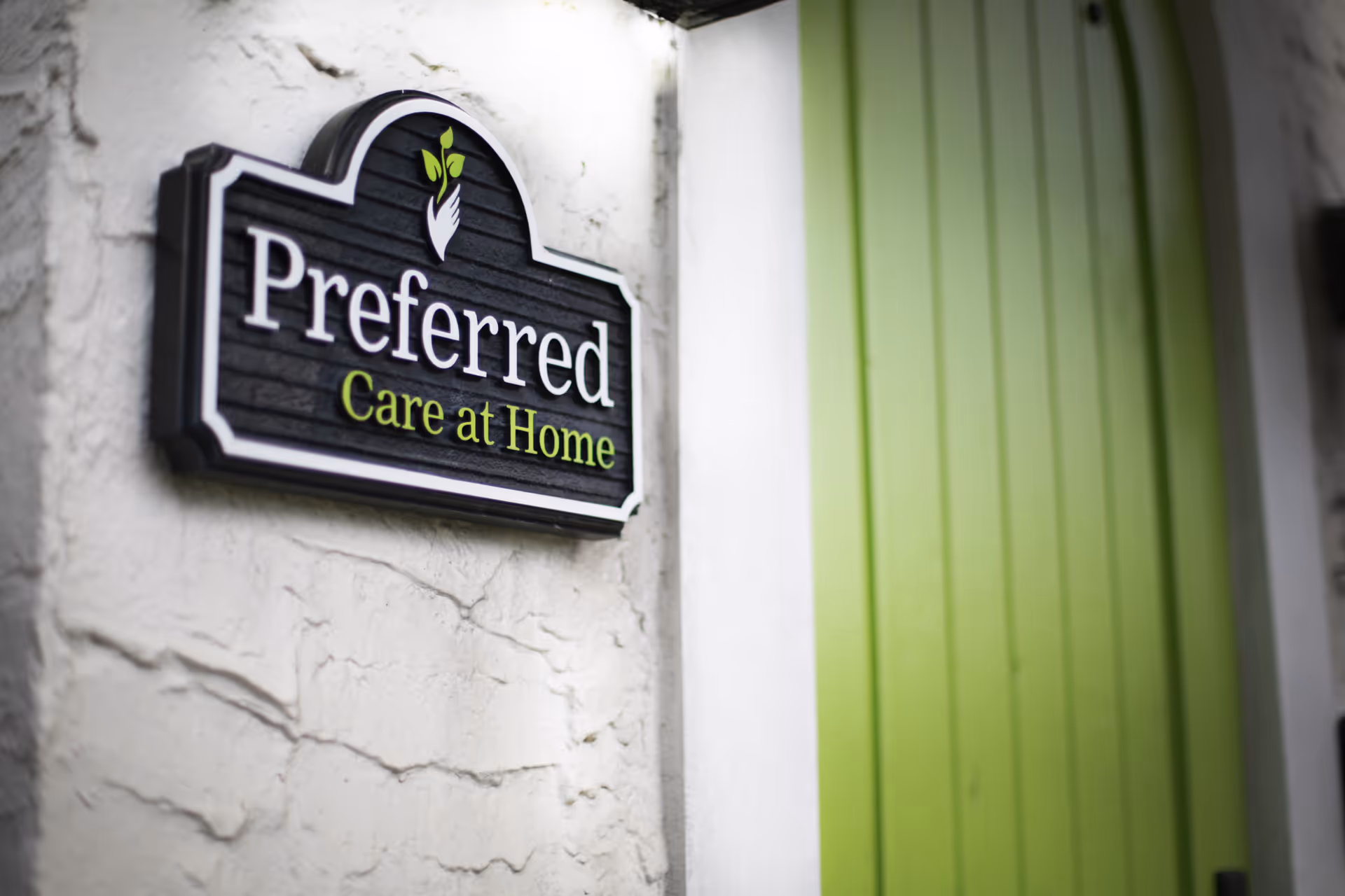 Exterior sign reading Preferred Care at Home on a textured wall beside a bright green door.