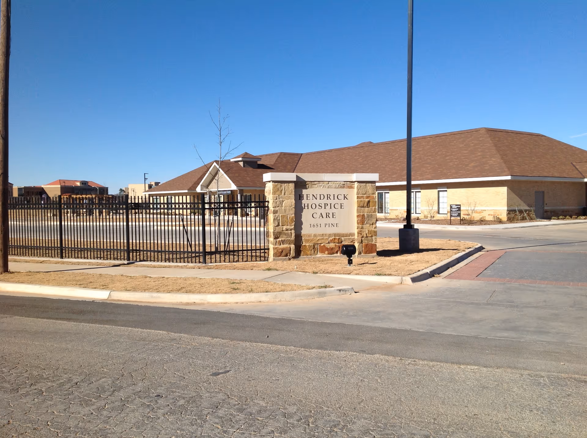 Exterior view of Hendrick Hospice Care facility with stone sign, fence, and entrance.