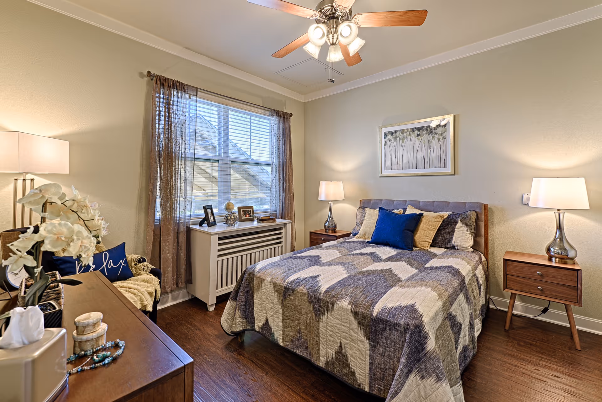 Cozy bedroom with a queen bed, two nightstands, lamps, and a window with sheer curtains.