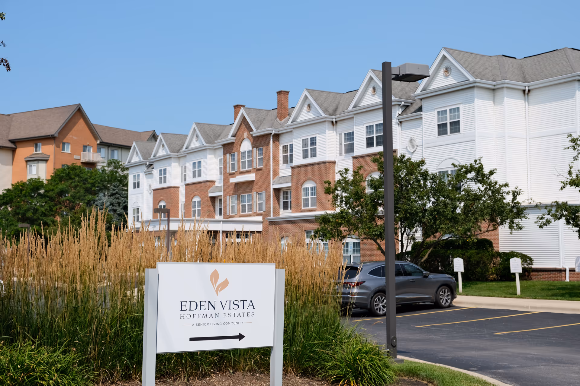 Exterior front view of the Eden Vista Hoffman Estates senior living building with its entrance sign and a parked car.