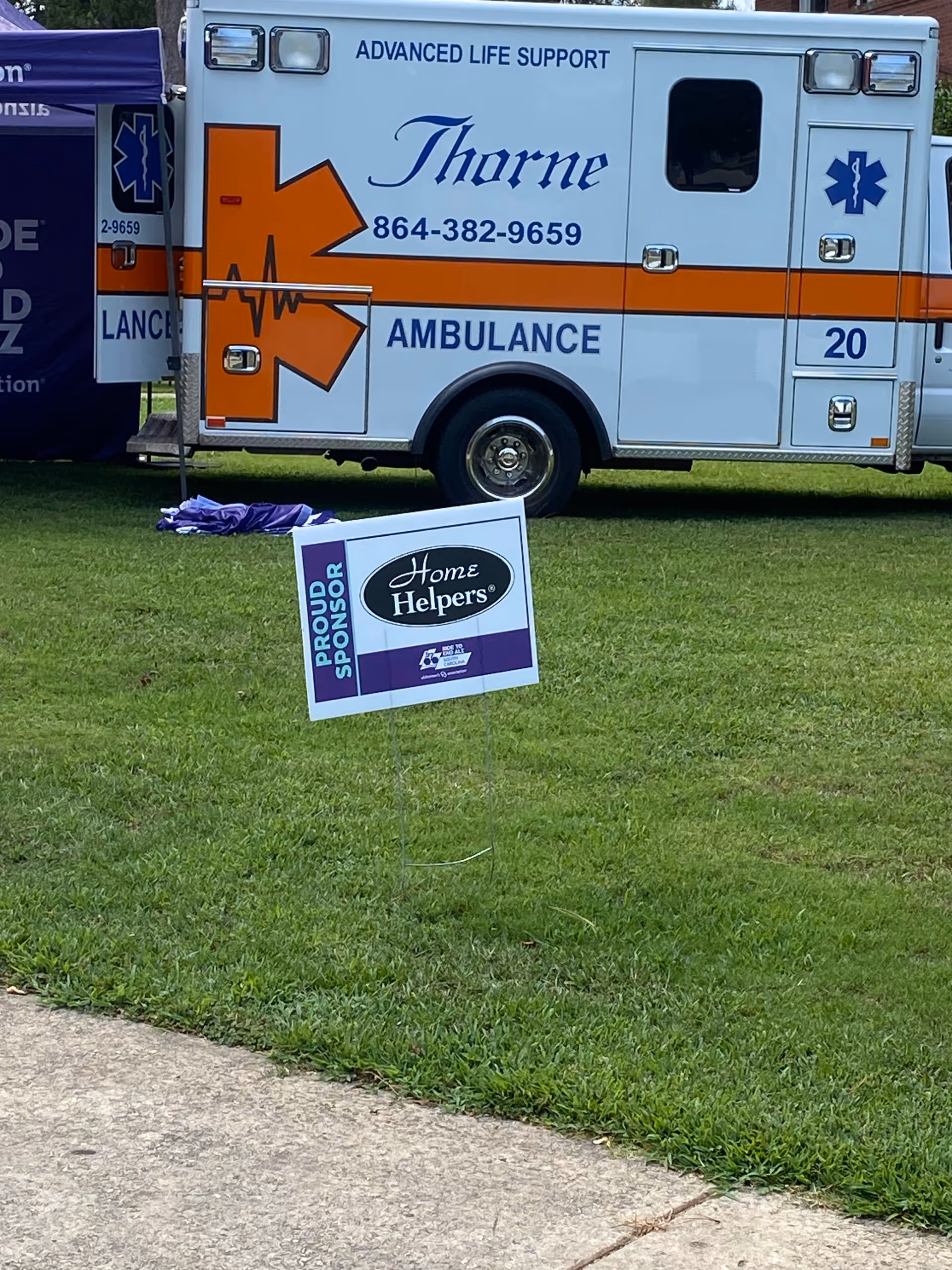 Ambulance parked on grass beside a Home Helpers sign outdoors.