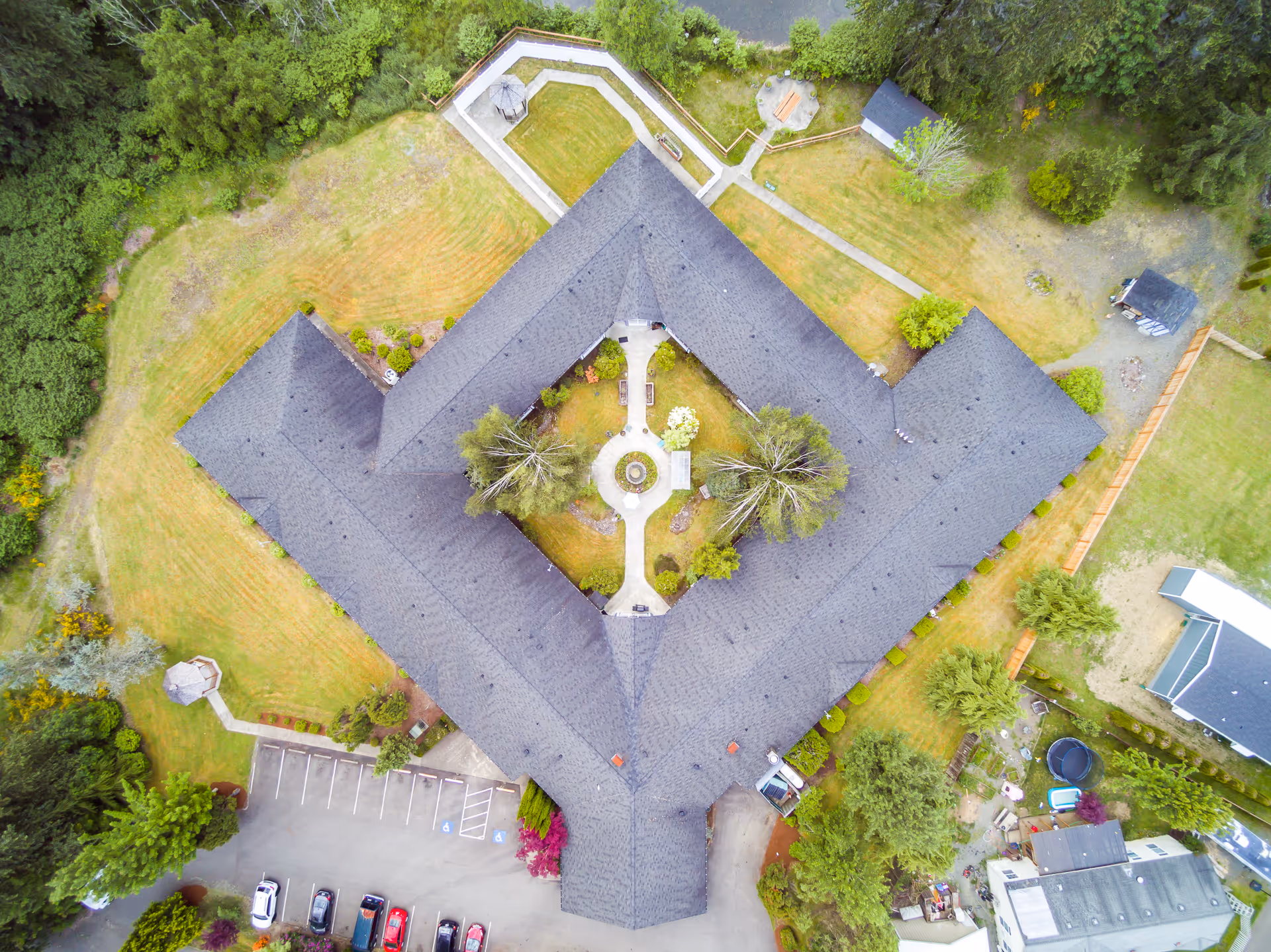 Aerial view of Heritage House Morton Assisted Living and Memory Care facility showing a large building with a central courtyard garden, surrounded by trees, parking spaces, and pathways.