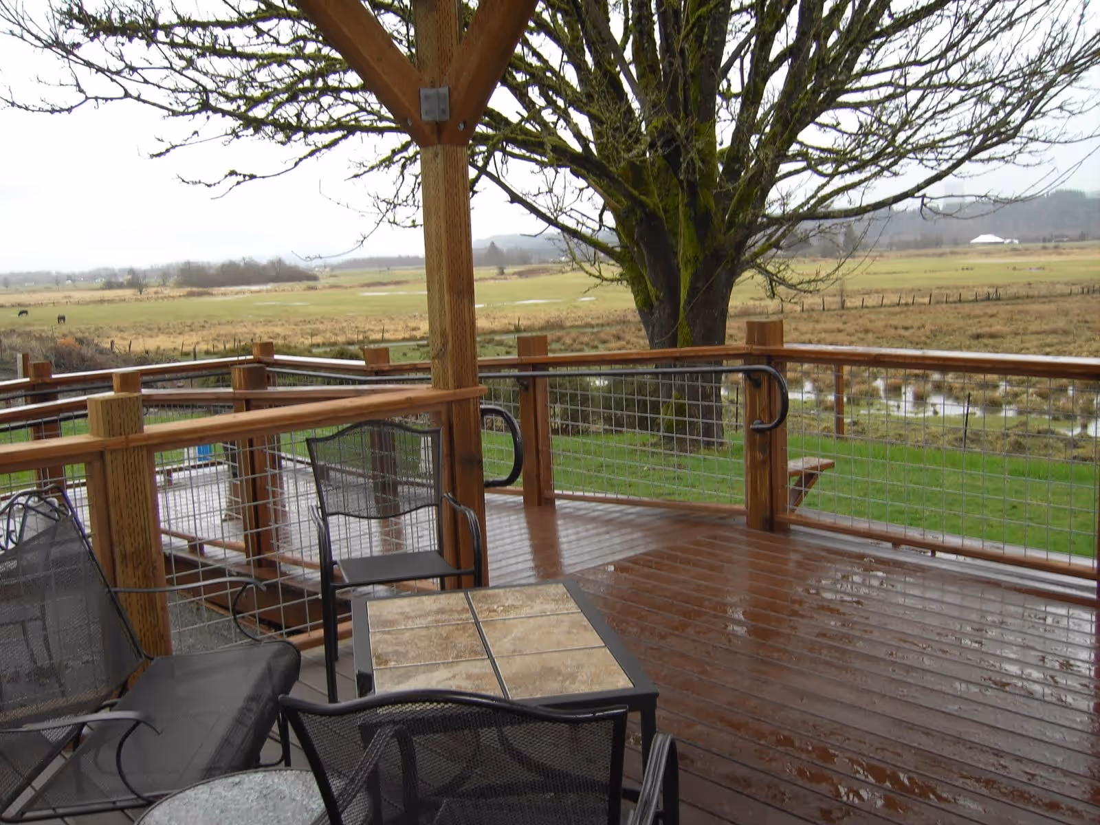 Wooden outdoor deck with chairs and table overlooking fields and distant trees.