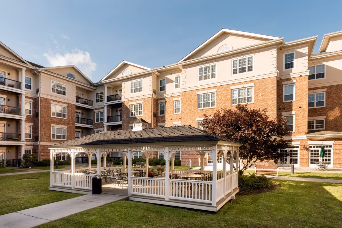 Multi-story brick senior living building with a white gazebo and courtyard seating under a blue sky.
