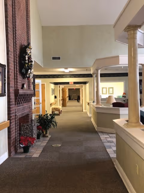 Long hallway inside Menorah House with a reception desk, columns, and potted plants.