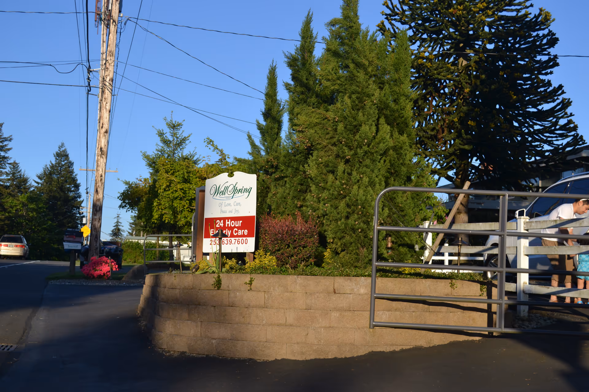 Exterior view of Wellspring 24 HR Elderly Care facility entrance with sign and trees.