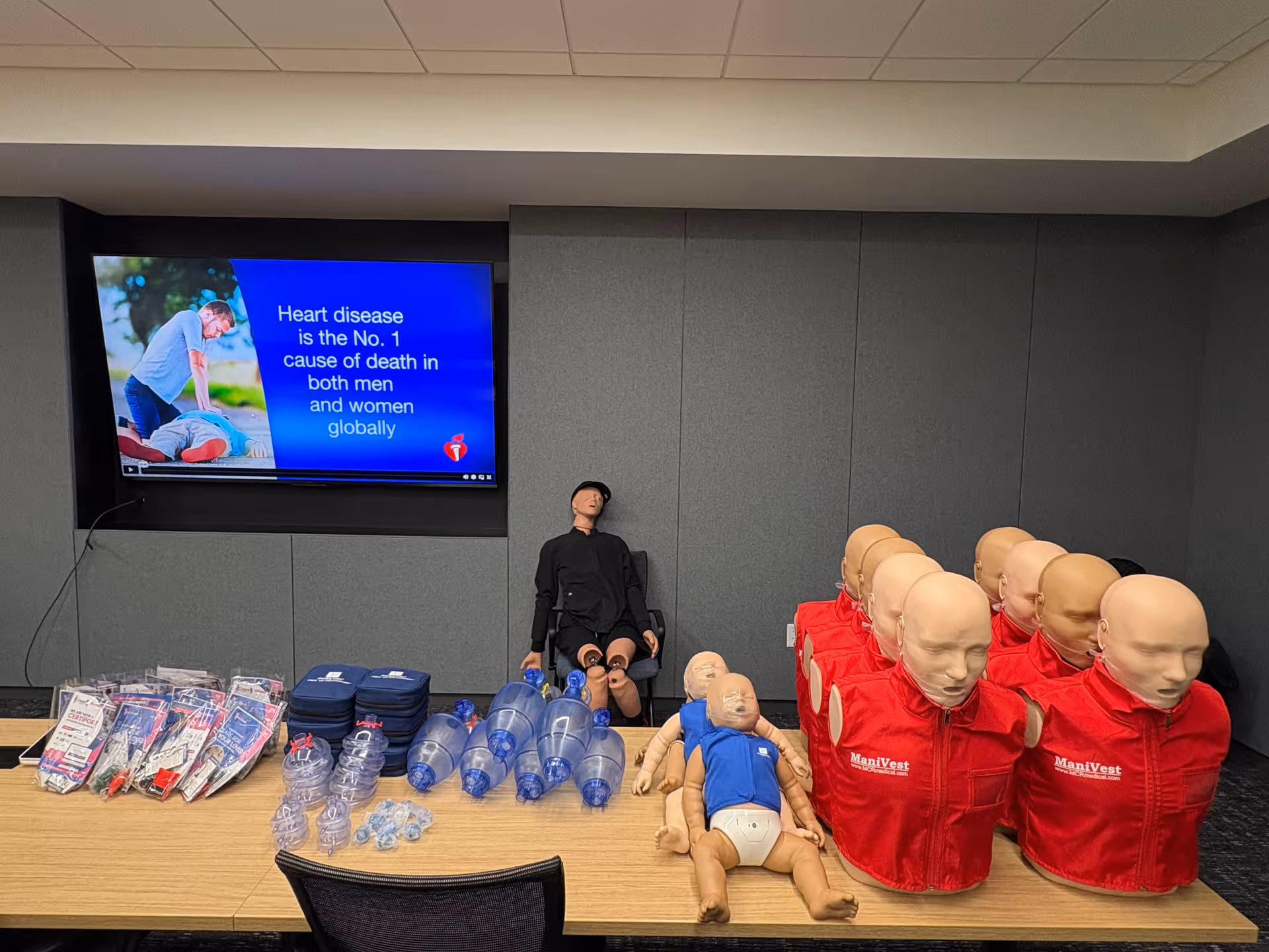 CPR training room with adult and infant mannequins beside a medical presentation screen