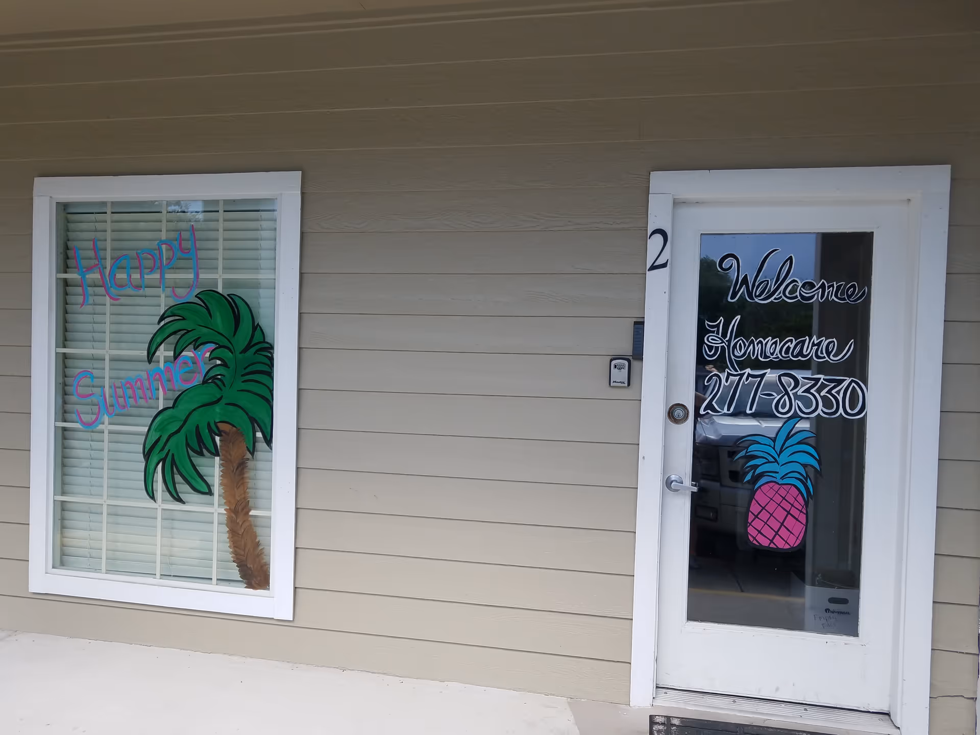 Exterior view of a beige building with a glass door and palm tree window art.