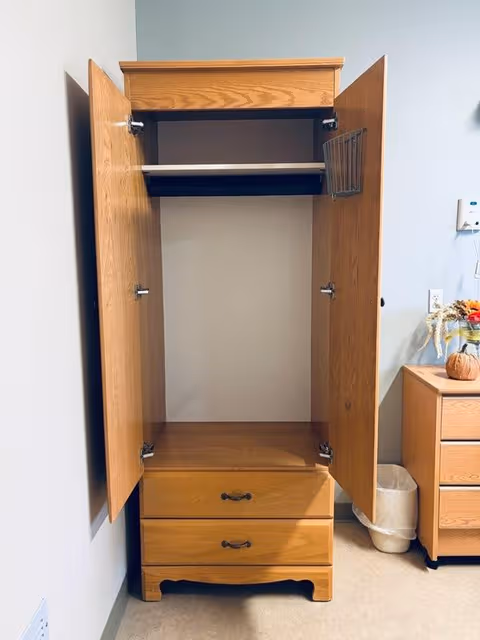 Open wooden wardrobe with shelves and drawers in a bedroom.