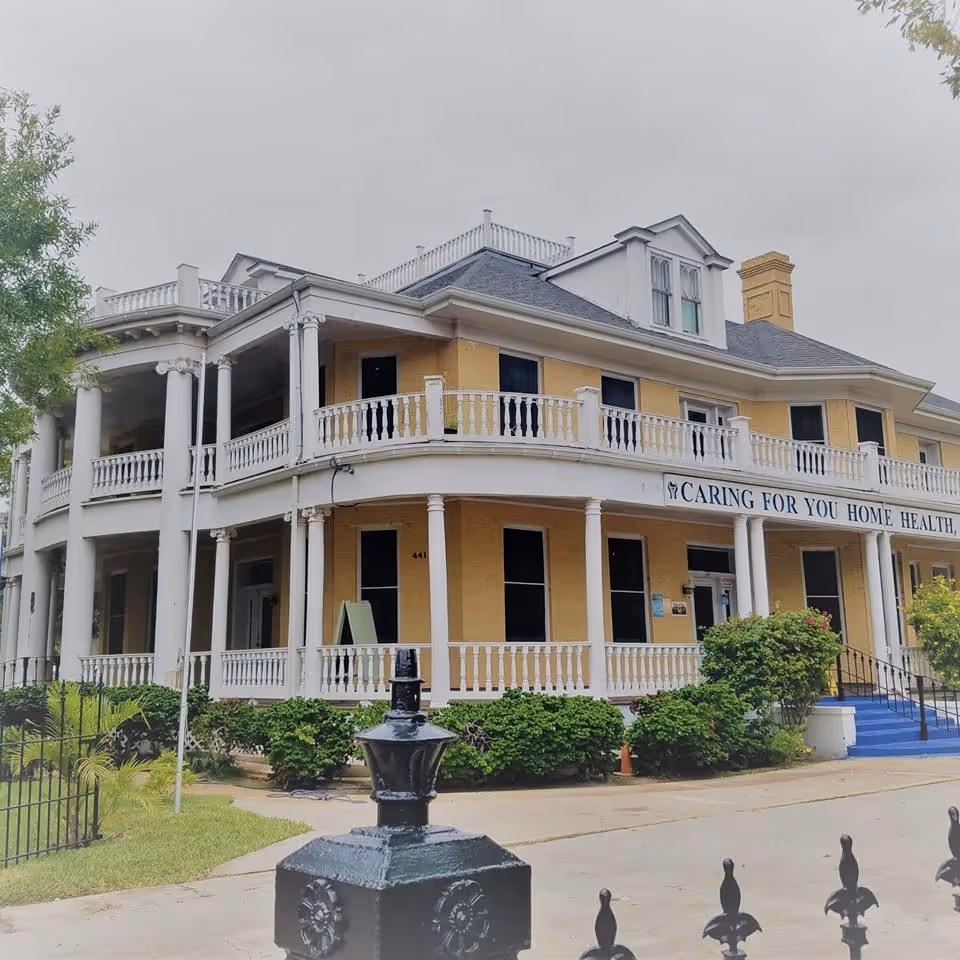 Two-story beige care facility exterior with white railings and a front entrance.