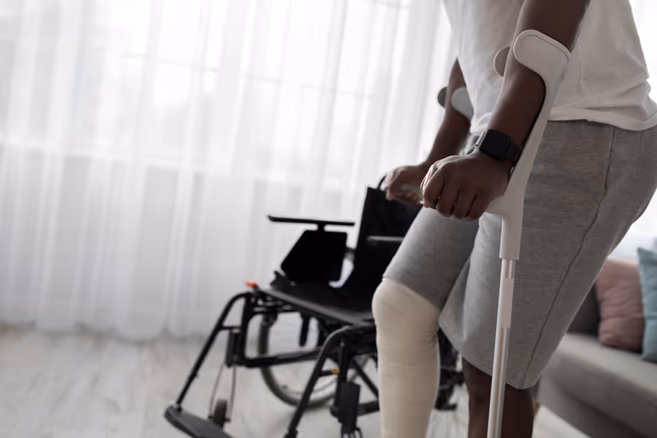 Person with a crutch beside a wheelchair in a bright living room.