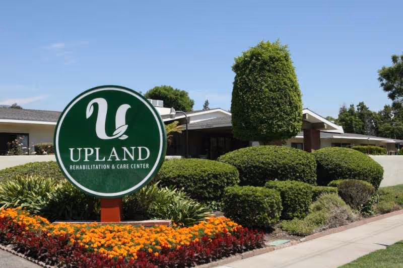 Front exterior view of Upland Rehabilitation & Care Center with a green sign and trimmed landscaping.