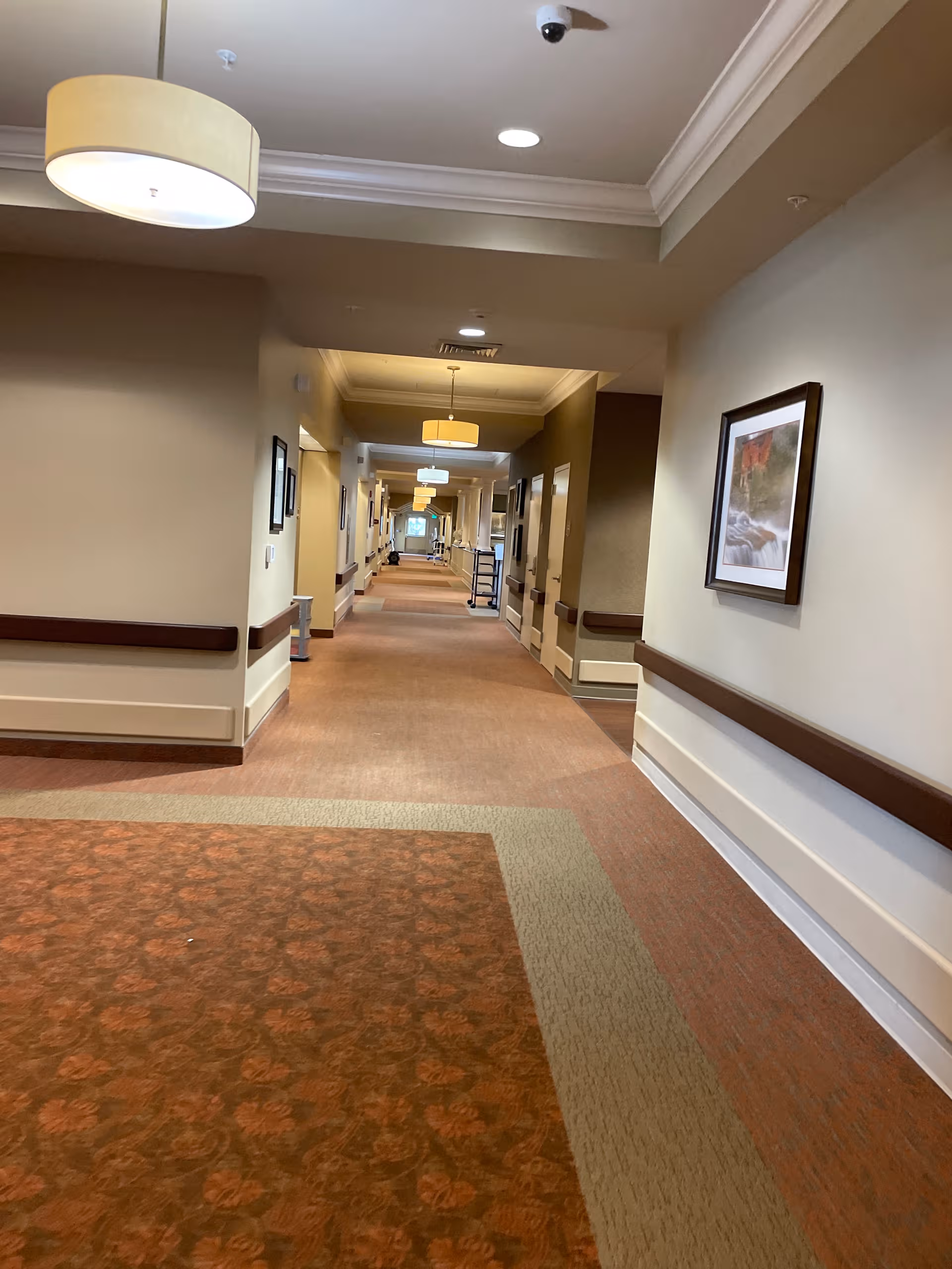 Long beige carpeted hallway in a senior living facility with framed art.