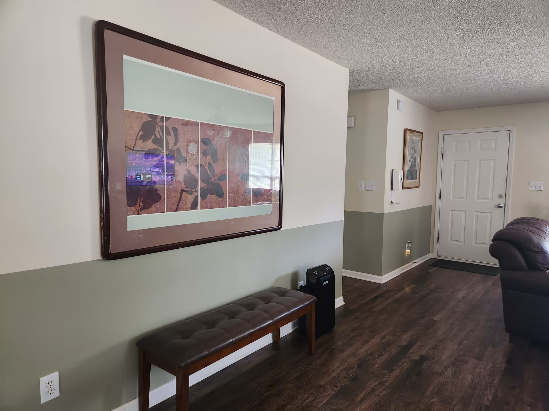 Two-tone lobby area with tufted bench, wall art, and doorway.