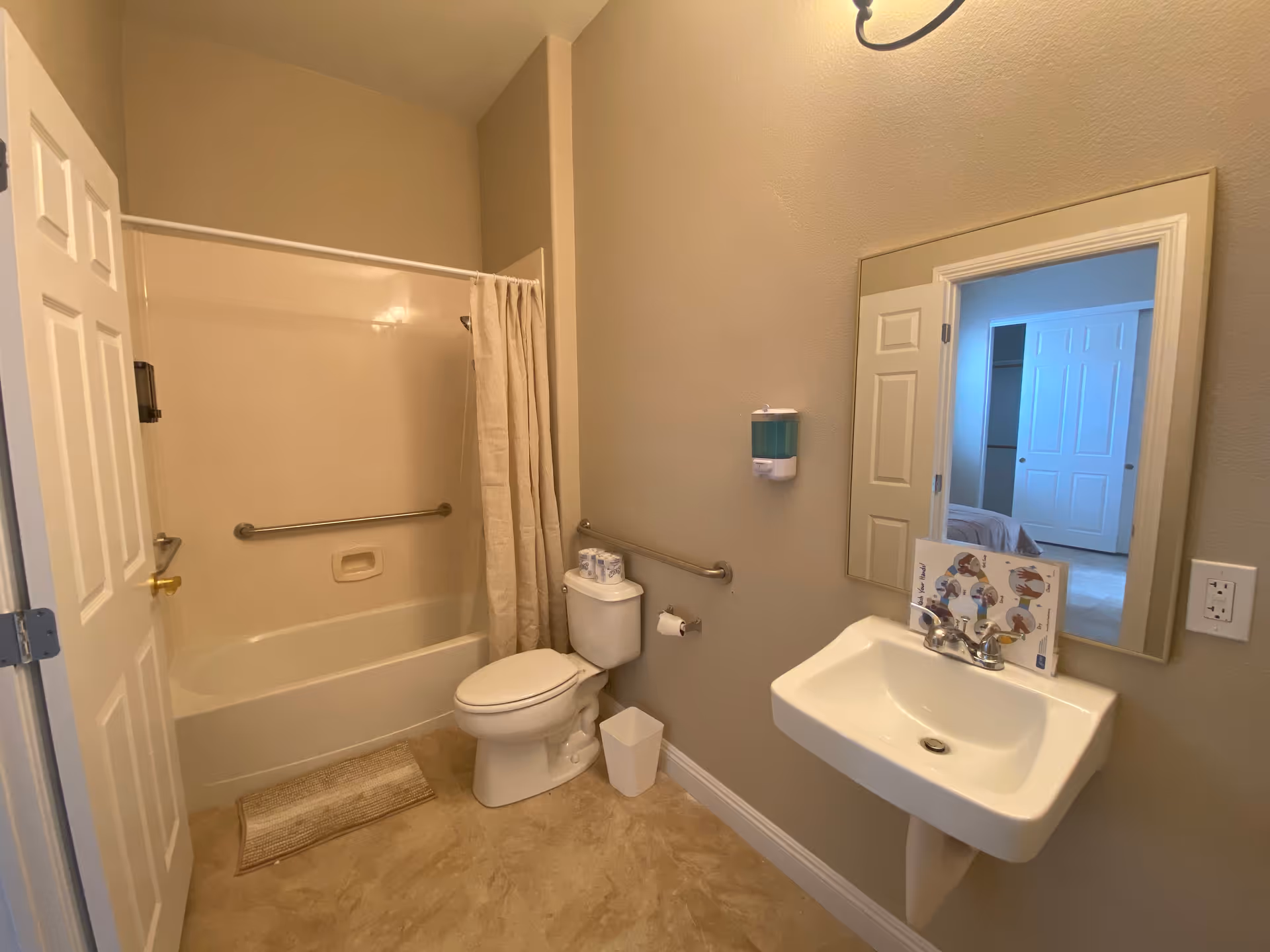 Accessible bathroom with bathtub, grab bars, toilet, sink, and wall mirror.