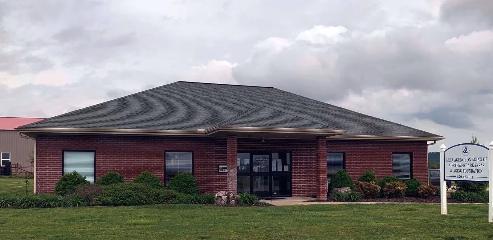 Brick facility with front entrance, well-kept shrubs, and aging office sign.