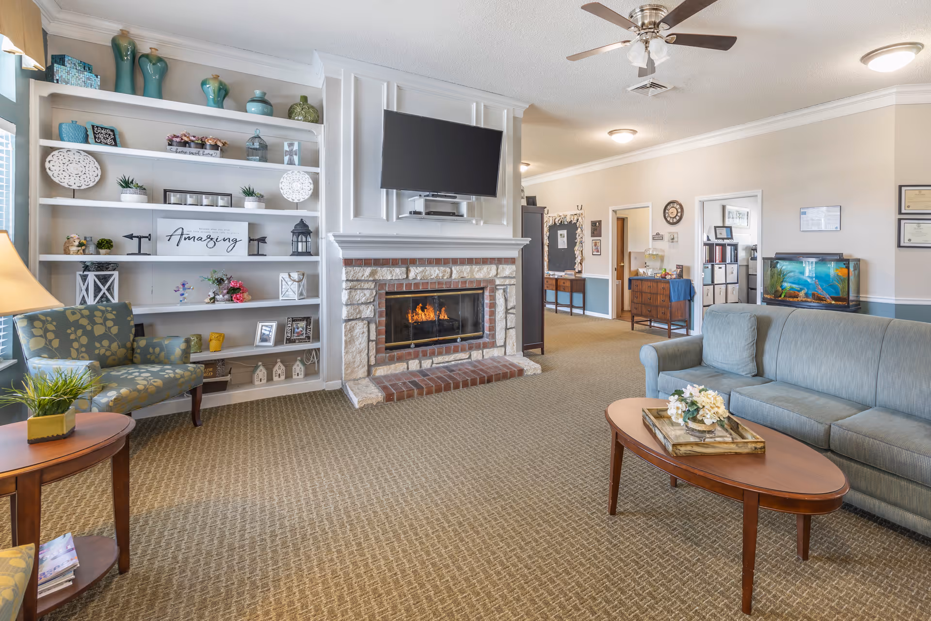 Cozy living room in a senior facility featuring a fireplace, built-in shelves, TV, and seating.