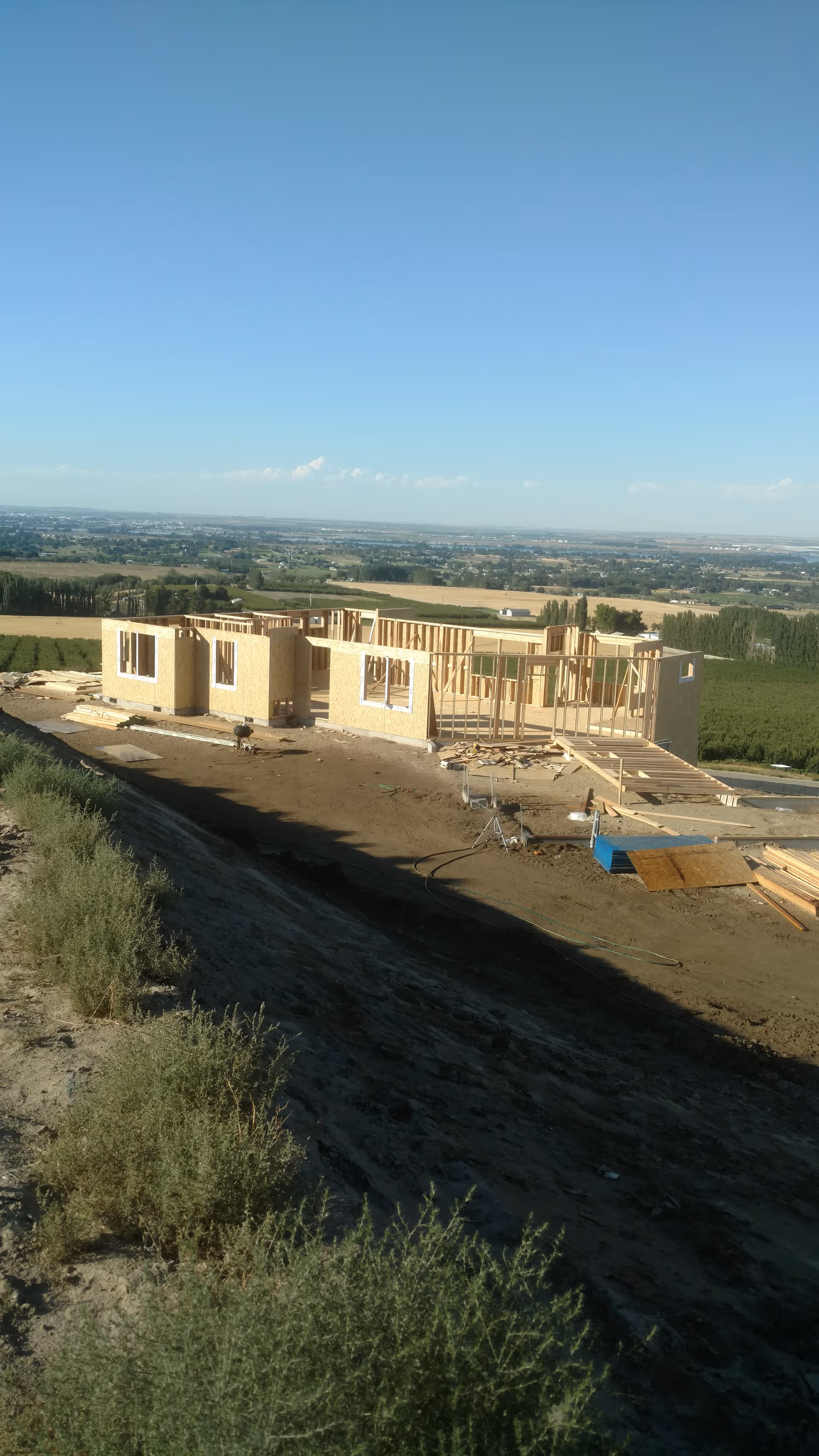 Under-construction single-story building on a hillside with wooden framing and equipment.