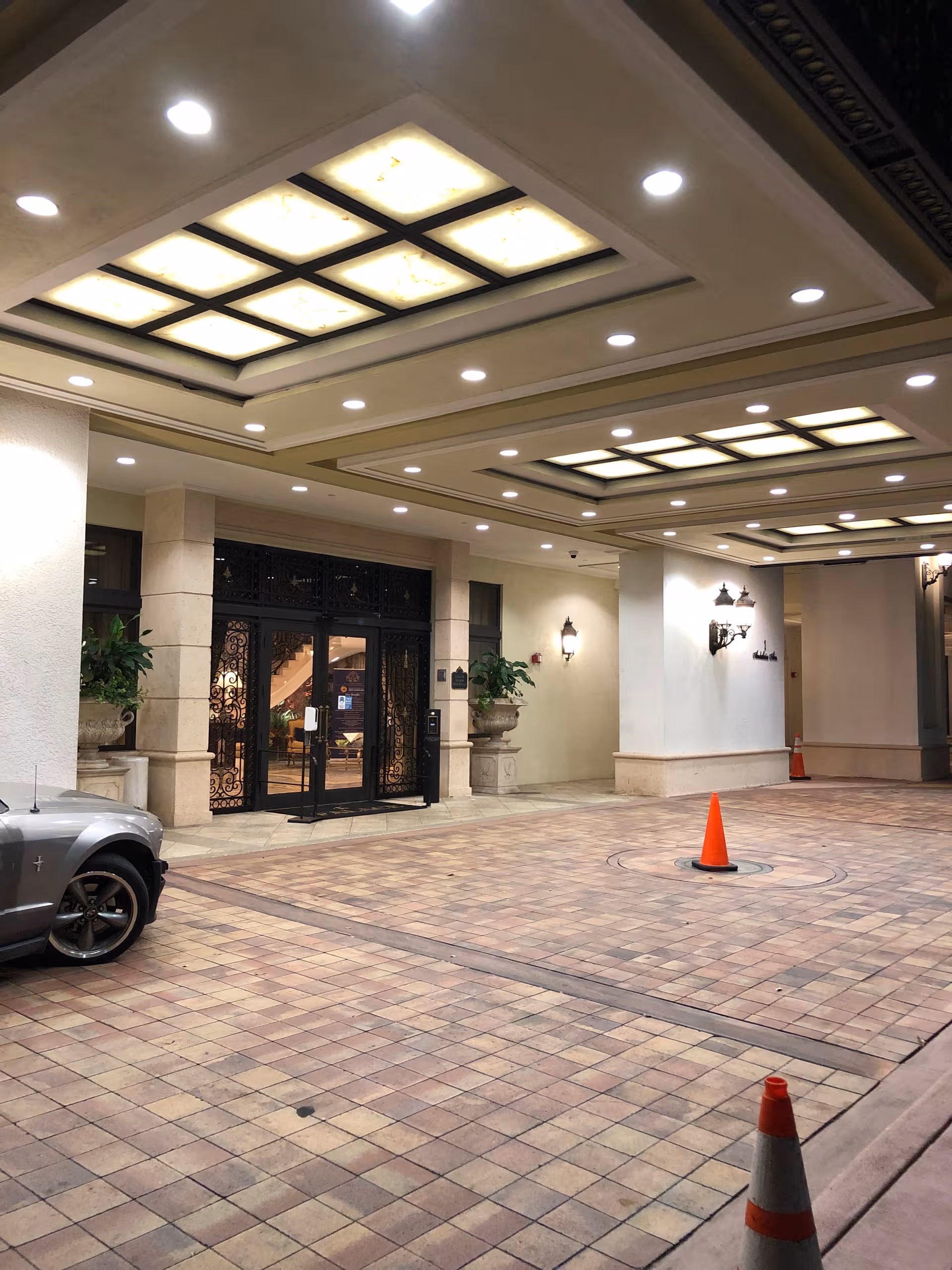 Covered entrance to The Palace at Coral Gables showing glass doors, arches, and a car.