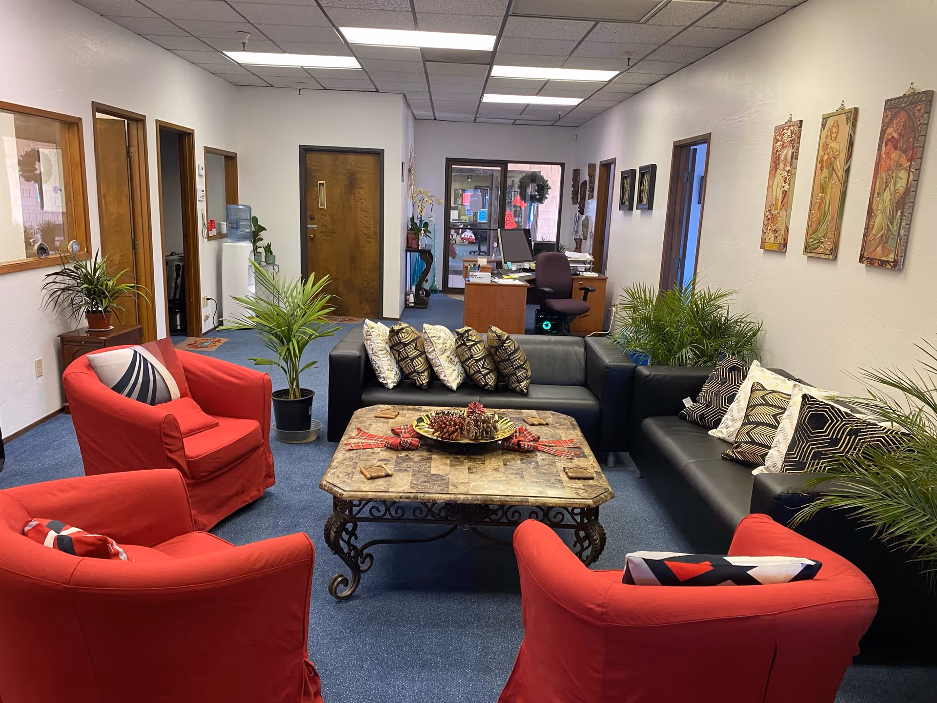 Cozy common living area with red chairs, black sofas, plants, and a coffee table.