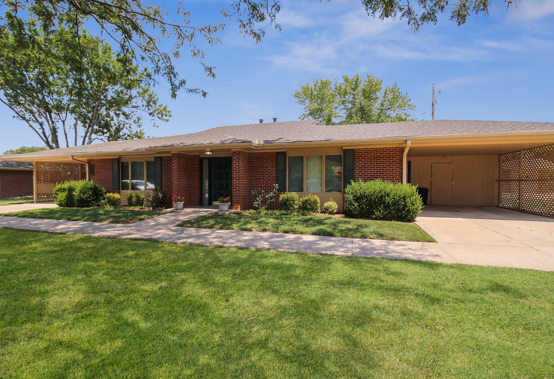 Single-story brick senior living facility with a green lawn, shrubs, and a carport on the right.