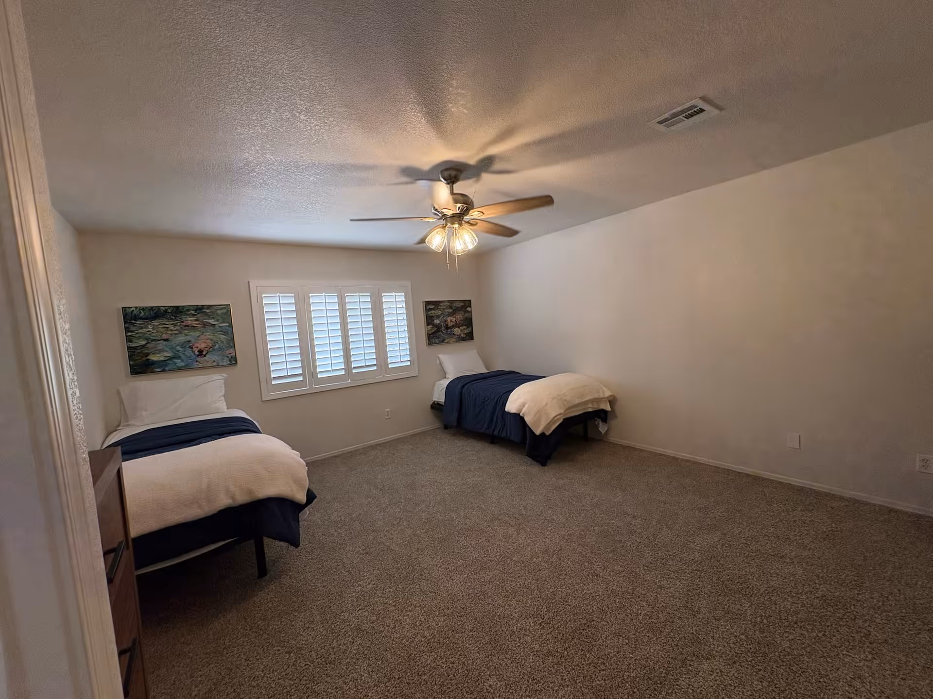 Two twin beds in a carpeted bedroom with a ceiling fan and window shutters.