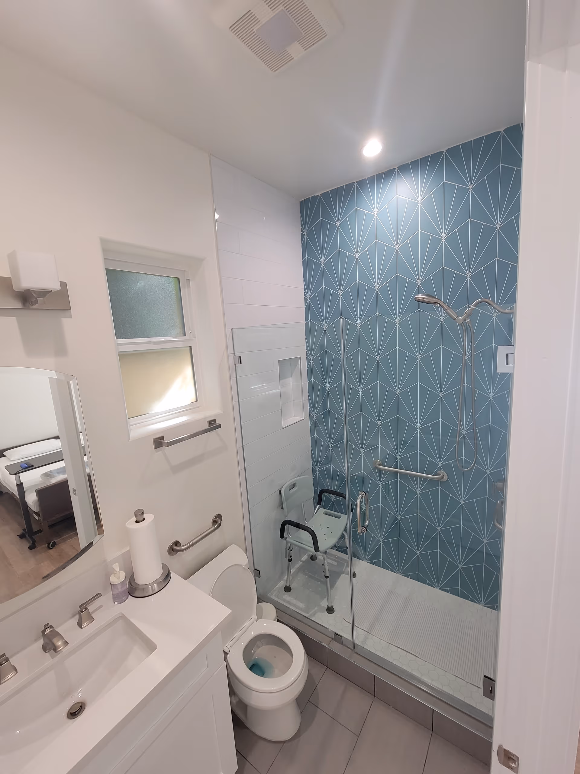 Accessible bathroom with glass-enclosed shower, blue geometric tiles, walker, and grab bars.